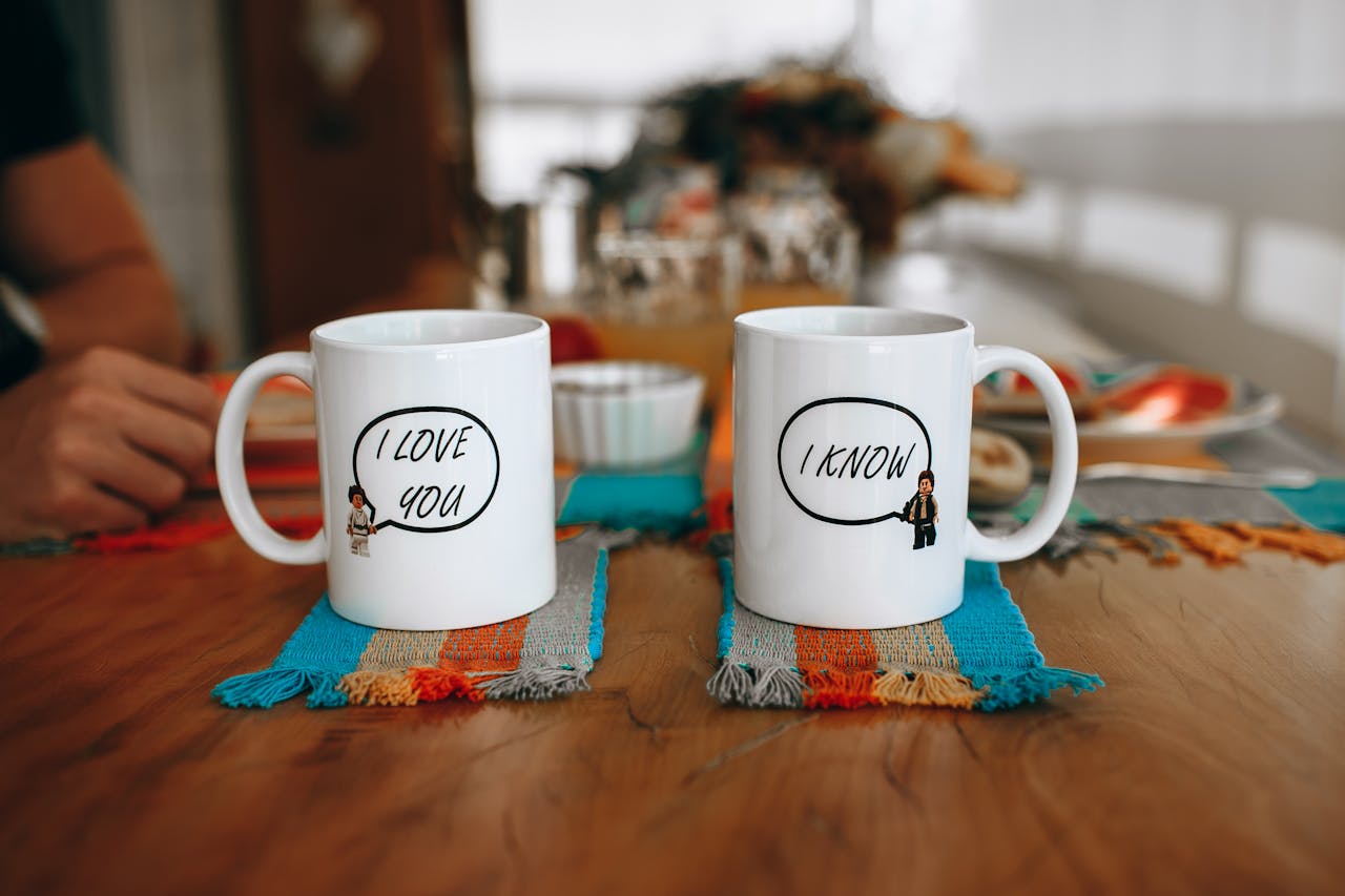 Two mugs with playful text on a table showcasing a cozy indoor setting.
