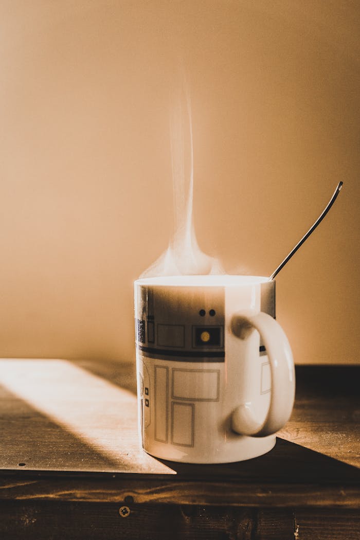 A steaming coffee mug with a unique design placed on a wooden table under warm morning light indoors.